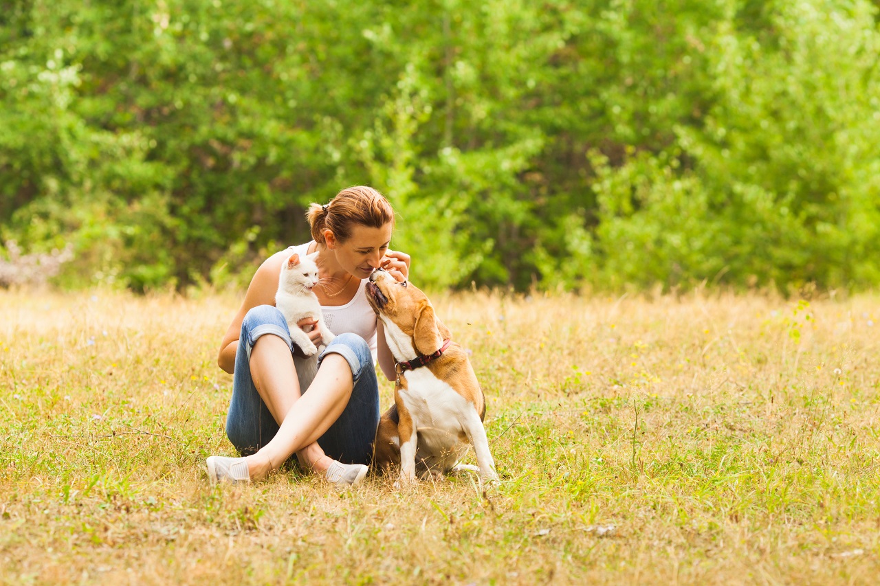 Eine Frau sitzt mit ihrem Hund in Wiese und freut sich, dass er seine Allergie überwunden hat